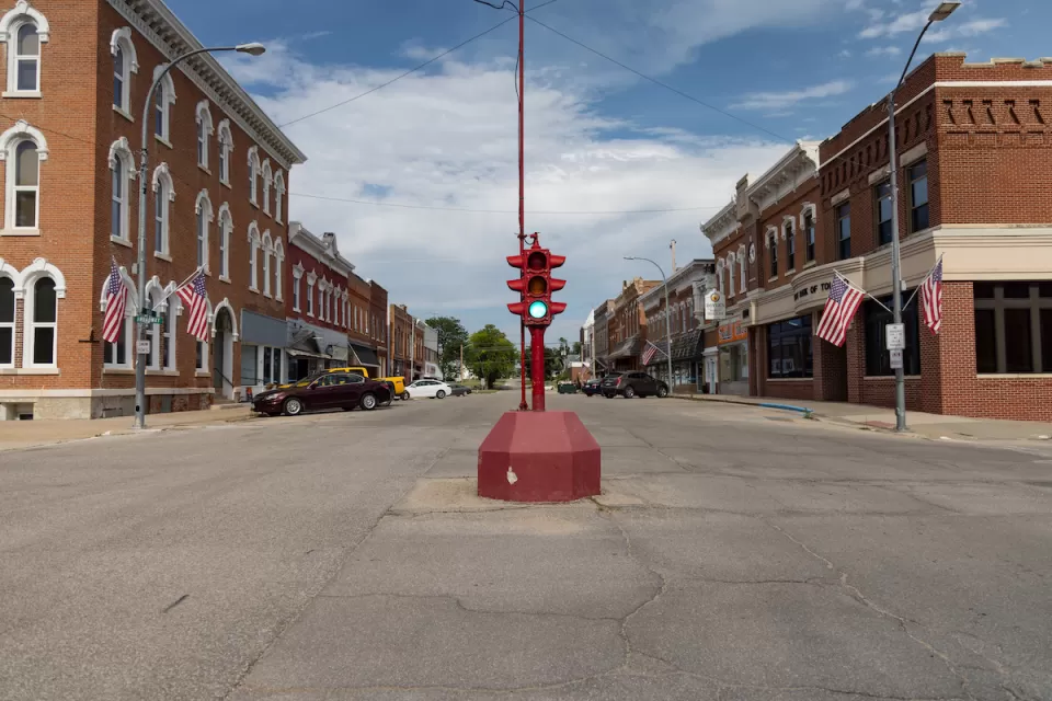Red antique stoplight in the middle of wide intersection flanked by brick buildings in downtown rural Toledo, Iowa